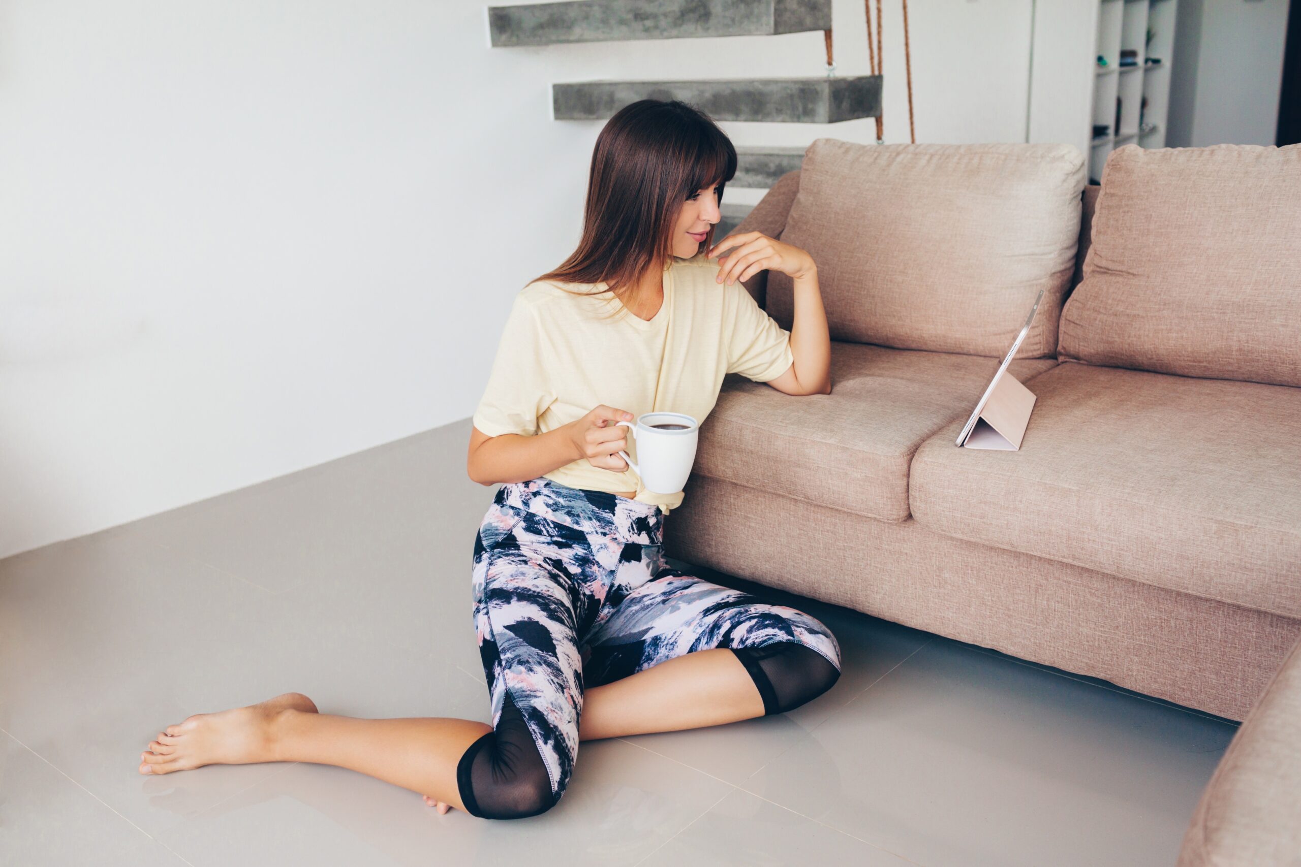 Happy woman in sportive wear  talking by mobile phone, sitting on the flooor in living room after training .